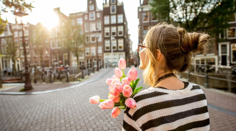 woman in striped black and white sweater with a messy bun and she's holding flowers while walking in amsterdam
